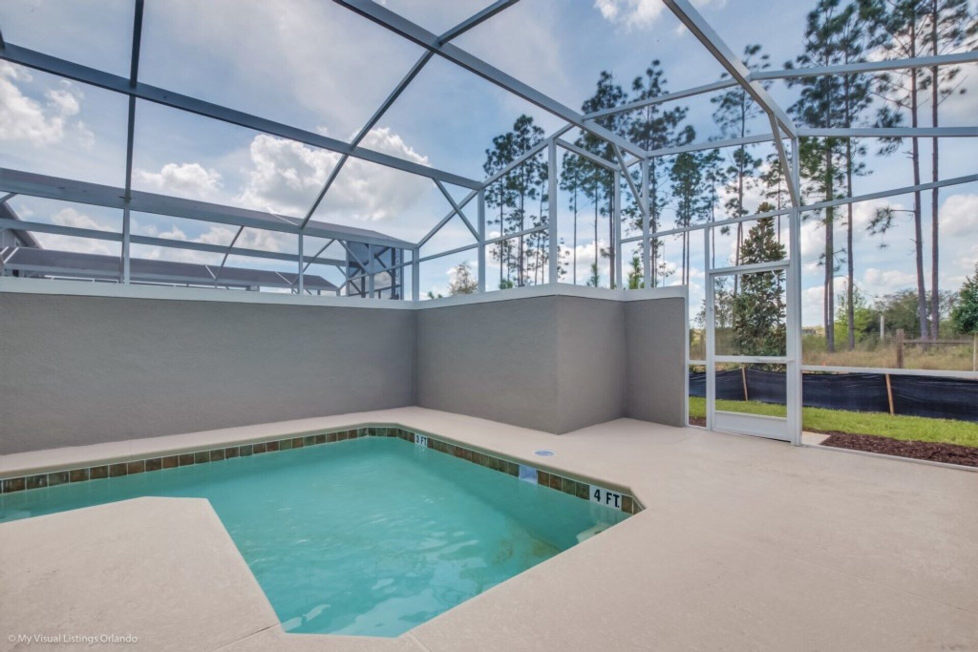Ein überdachter Pool mit Glasdach, umgeben von einer Betonplattform und Blick auf Bäume.