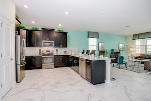A modern kitchen with dark cabinets, a central island, and a dining area with blue chairs.