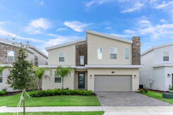 A modern two-story residential building with a garage, a stone accent wall, and a well-maintained front lawn.