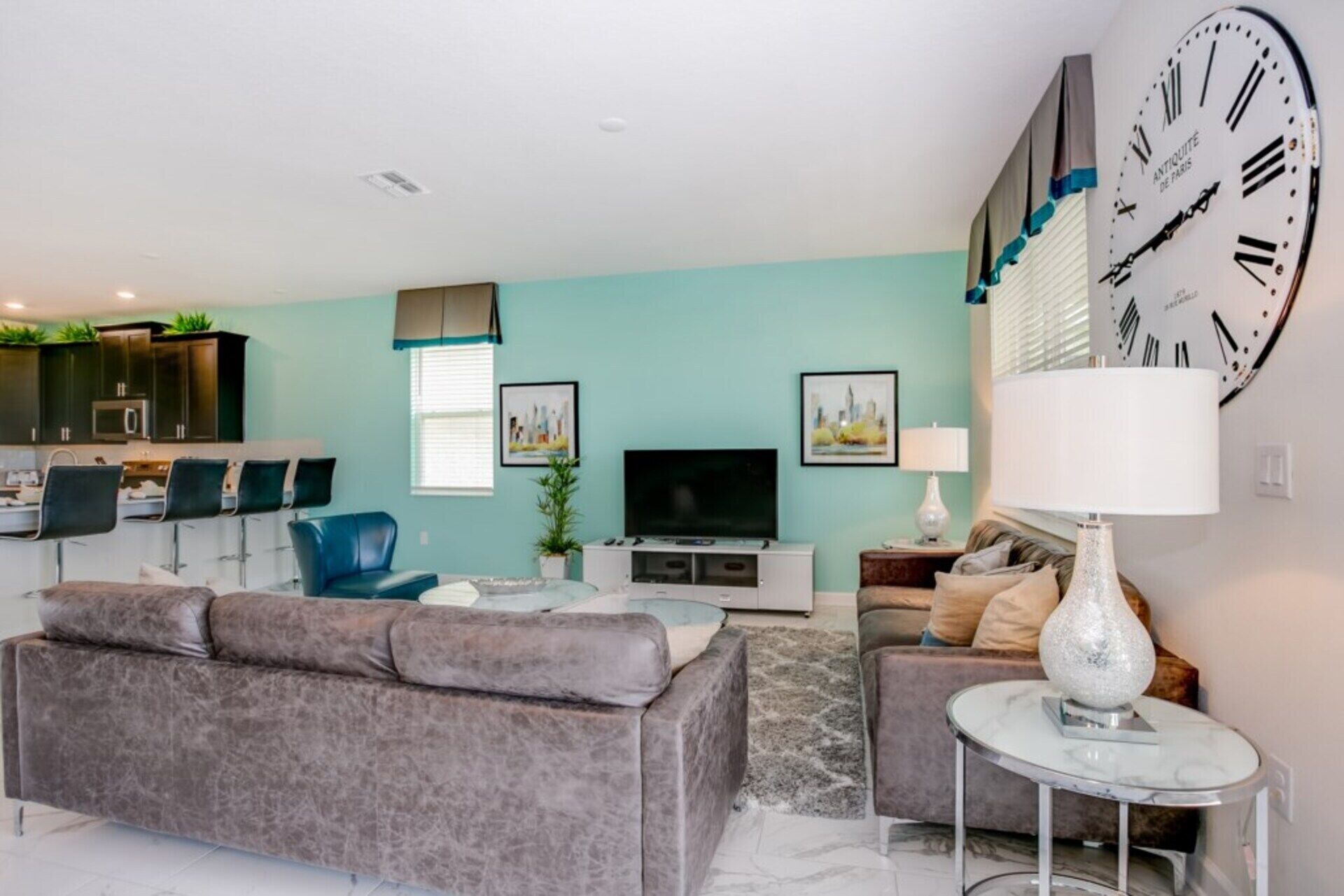A modern living room with a grey sofa, a TV, and a clock on the wall.