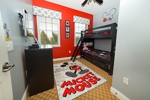 Une chambre d’enfant avec un lit superposé, une décoration sur le thème de Mickey Mouse et une fenêtre avec des stores.