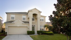 A two-story residential building with a beige facade, a central entrance with a small porch, and a garage. - Villa in Windsor Hills Resort 1407 (Kissimmee)