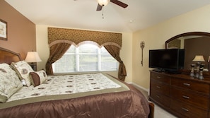 A bedroom with a bed, a dresser, a television, and a ceiling fan.