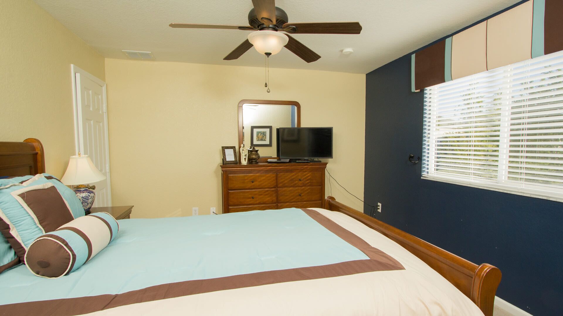 A bedroom with a bed, a dresser, a television, and a ceiling fan.
