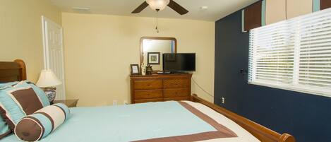 A bedroom with a bed, a dresser, a television, and a ceiling fan.