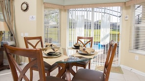 A dining area with a glass table, wooden chairs, and a clock on the wall.