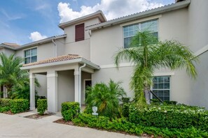 A two-story residential building with a covered patio, palm trees, and well-maintained landscaping.