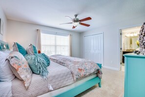A bedroom with a bed, a ceiling fan, a window with blinds, a door, and a dresser.