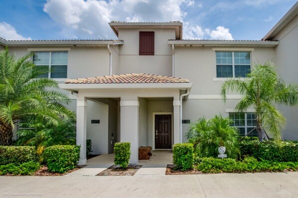 A two-story house with a covered porch, palm trees, and a well-maintained lawn.