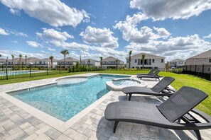A swimming pool with lounge chairs and a hot tub, surrounded by houses and a clear sky.