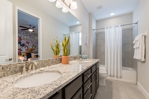 A bathroom with a granite countertop, two sinks, a shower with a glass door, and a ceiling fan.