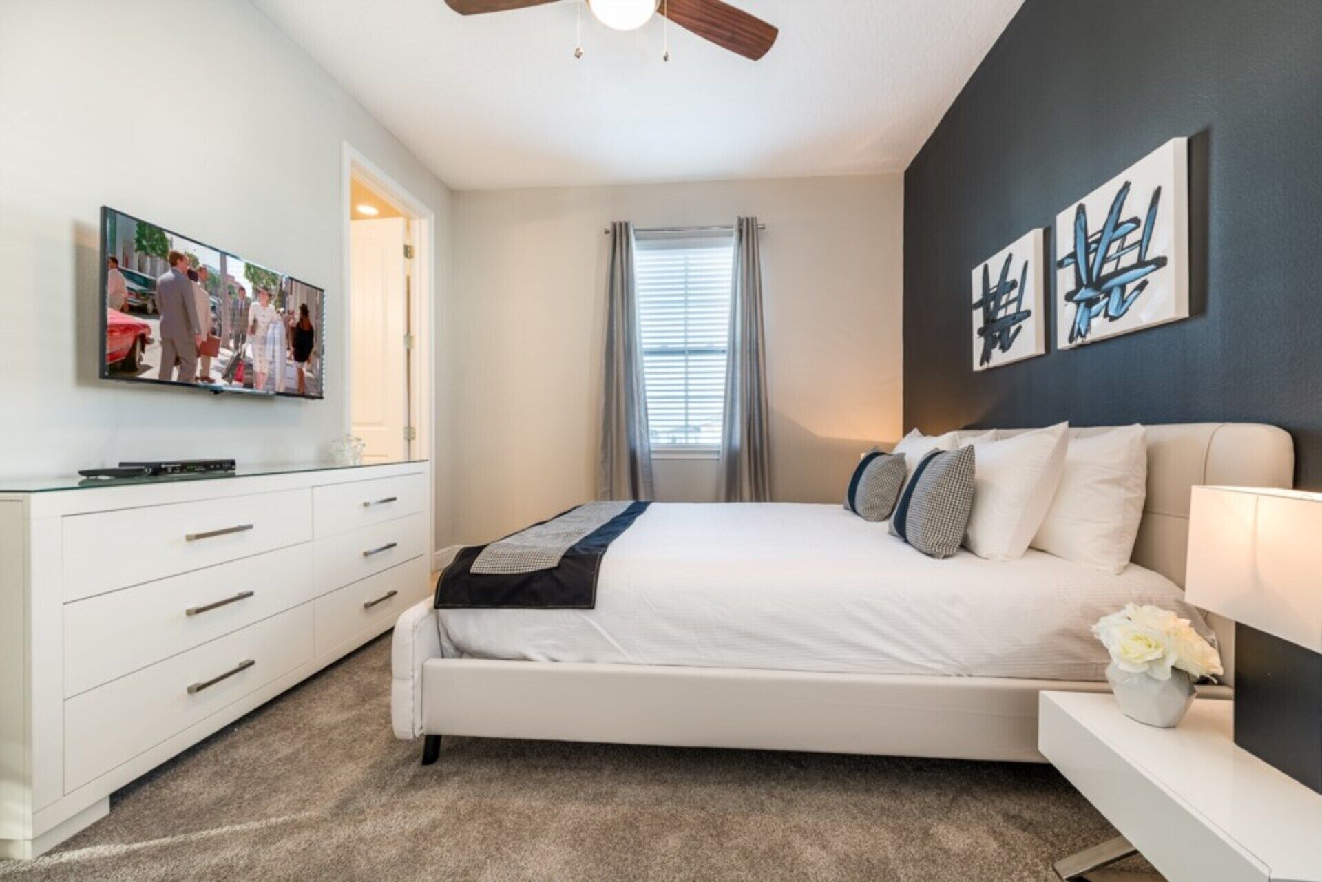 A bedroom with a bed, a dresser, a TV, and artwork on the wall.