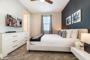 A bedroom with a bed, a dresser, a TV, and artwork on the wall.