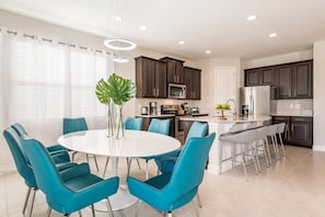 Una cocina moderna con armarios oscuros, una isla blanca y sillas azules alrededor de una mesa central.