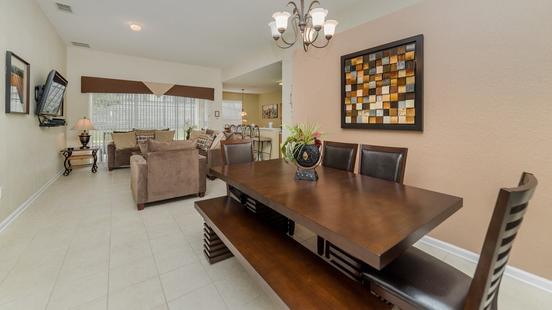 A spacious dining area with a large wooden table, cushioned chairs, and a chandelier.