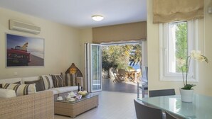 Un salon avec un canapé, une table basse et une table à manger en verre. Il y a une fenêtre avec des rideaux et une vue sur l’extérieur.