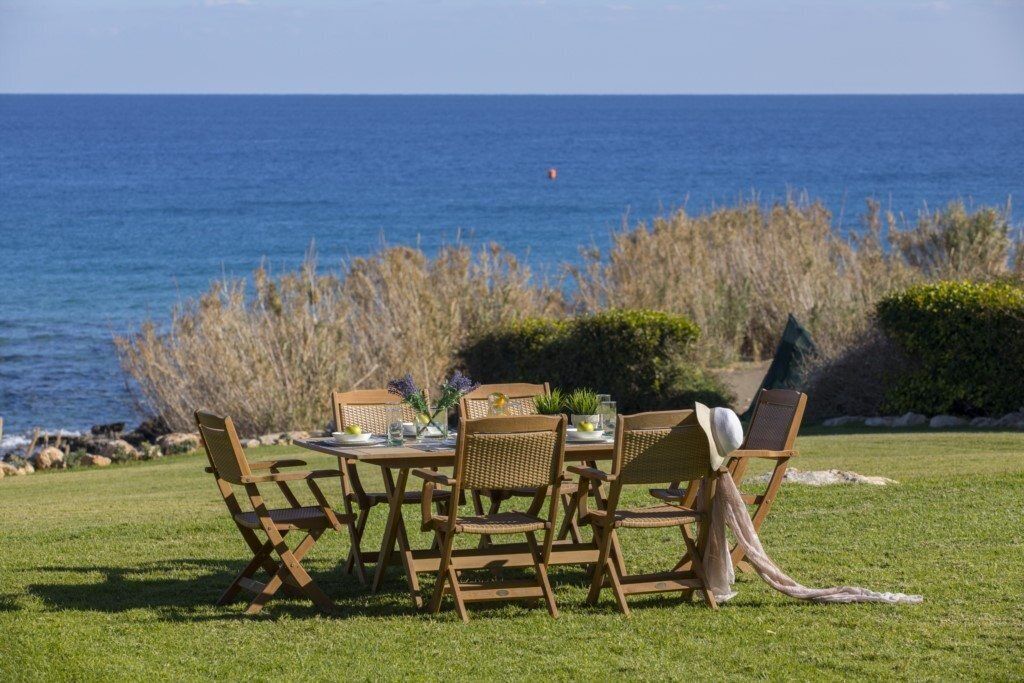 Un espacio exterior para comer con vista al océano, con mobiliario de mimbre y una mesa preparada para dos.