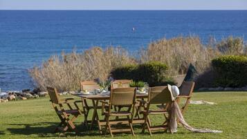 Un espacio exterior para comer con vista al océano, con mobiliario de mimbre y una mesa preparada para dos.