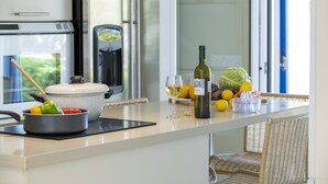 Une cuisine équipée d’une cuisinière, d’une machine à café, d’une bouteille de vin, ainsi que de divers fruits et légumes disposés sur le plan de travail.