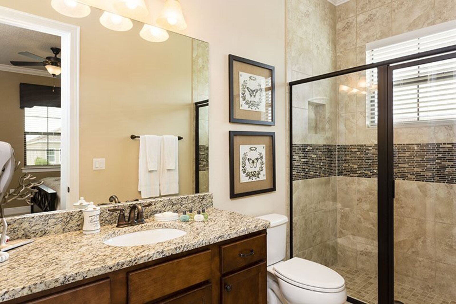 A bathroom with a granite countertop, a sink, a toilet, and a shower area. There are framed pictures on the wall and a towel rack with towels.