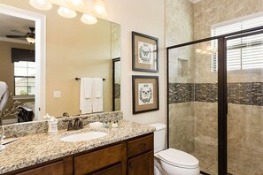 A bathroom with a granite countertop, a sink, a toilet, and a shower area. There are framed pictures on the wall and a towel rack with towels. - Rent a Luxury Villa on Reunion Resort, Minutes From Disney, Orlando Villa 3556 (Kissimmee)