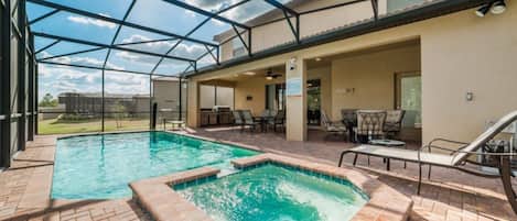 A covered outdoor swimming pool area with a hot tub, lounge chairs, and a patio with a ceiling fan.