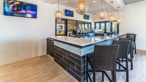 A bar area with a counter, multiple hanging light fixtures, and a television screen displaying a colorful image. - Beautiful Villa With Private Pool, Close to Disney, Orlando Villa 1835 (Kissimmee)