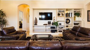A modern living room with leather sofas, a flat-screen TV, and a bookshelf with decorative items.