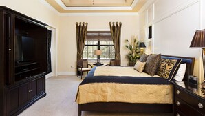 A bedroom with a large bed, a television, a ceiling fan, and a window with curtains.