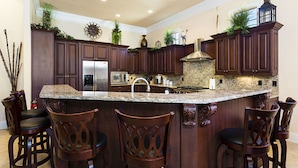 A spacious kitchen with dark wood cabinets, a granite island, and bar stools.