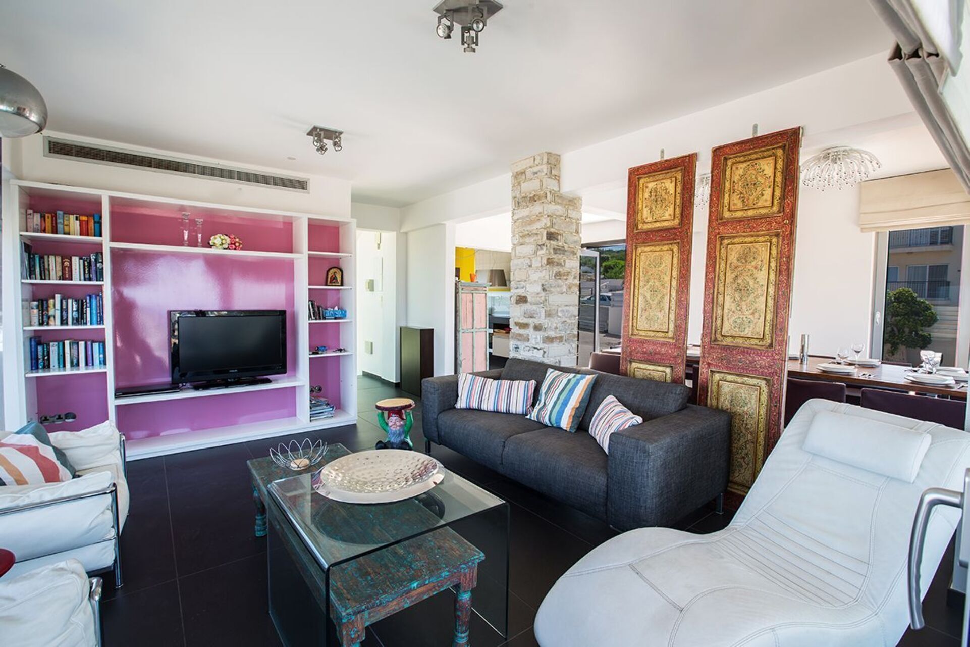 A modern living room with a TV, bookshelves, a sofa, and a dining area with a view.