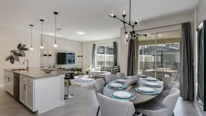 A modern kitchen with a central island, dining area with round table, and large windows offering a view. - Rent a Luxury Townhome on Storey Lake Resort, Minutes From Disney, Orlando Townhome 3224 (Kissimmee)