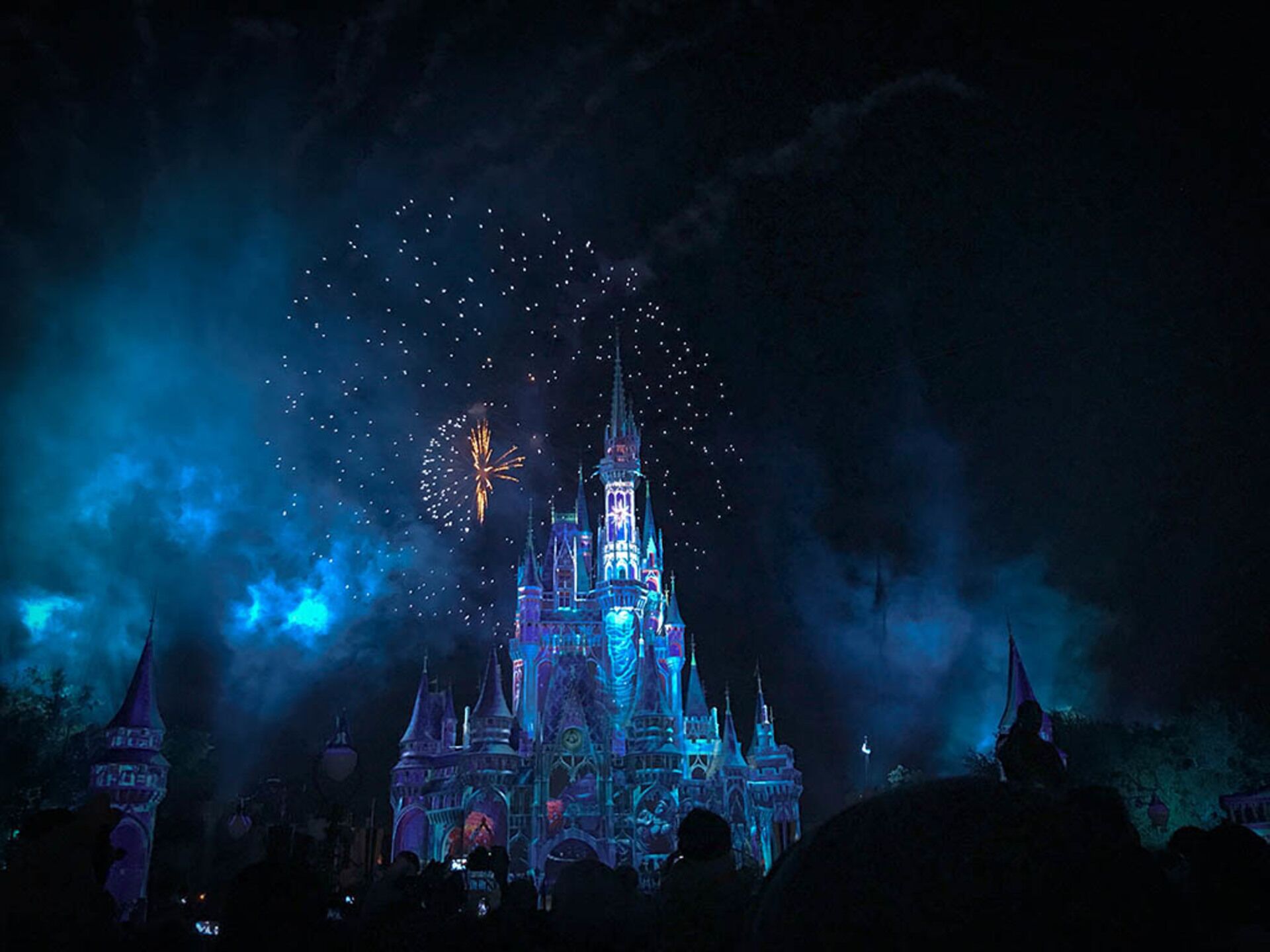 Uma construção semelhante a um castelo, com múltiplas torres e uma torre central, iluminada por luzes azuis e brancas.