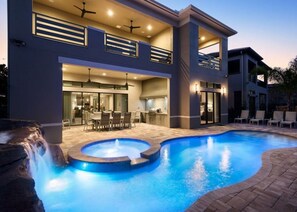 Una casa moderna de dos pisos amb piscina, zona de menjador exterior i una cascada.