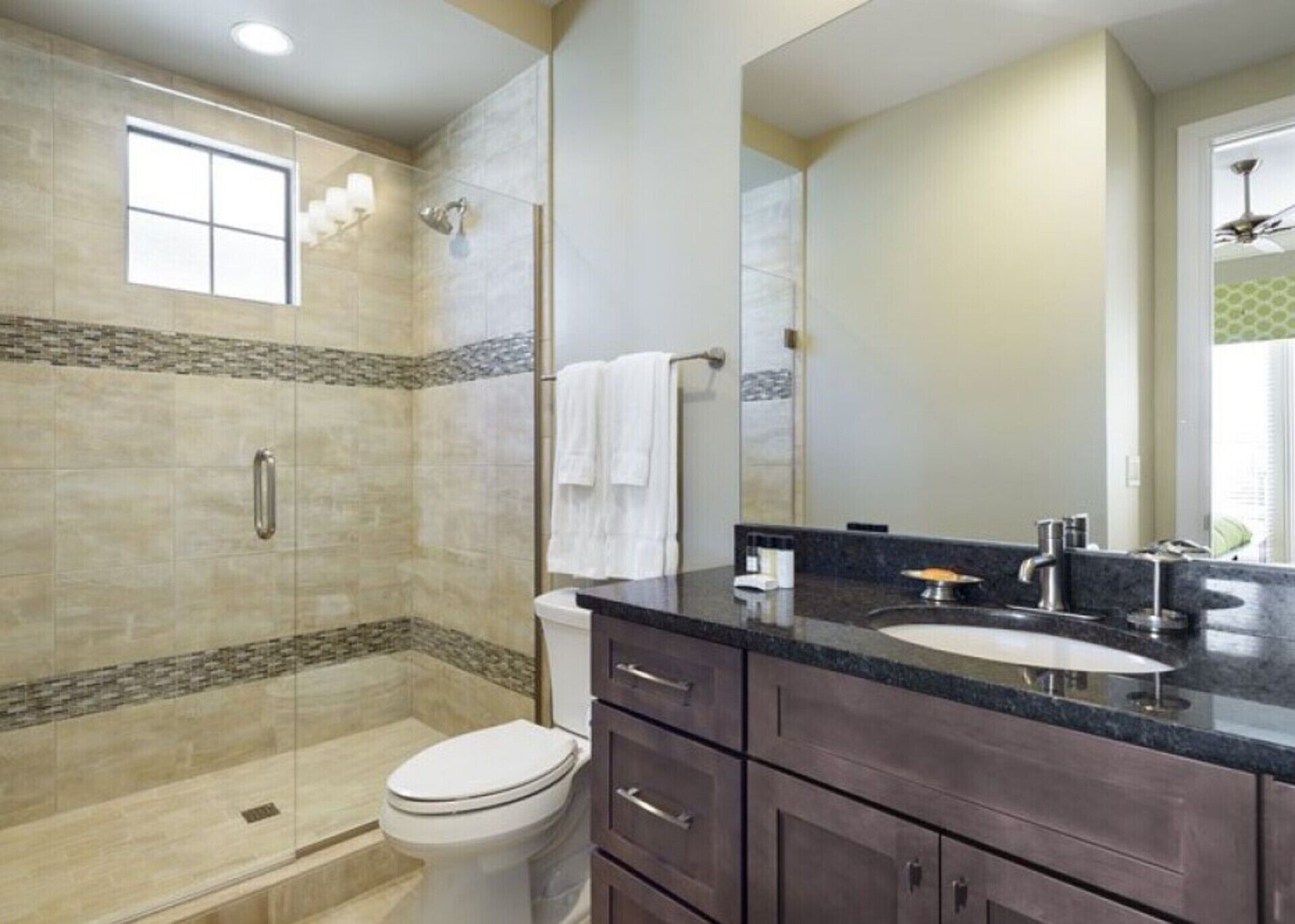 A bathroom with a shower, toilet, vanity, and a large mirror.