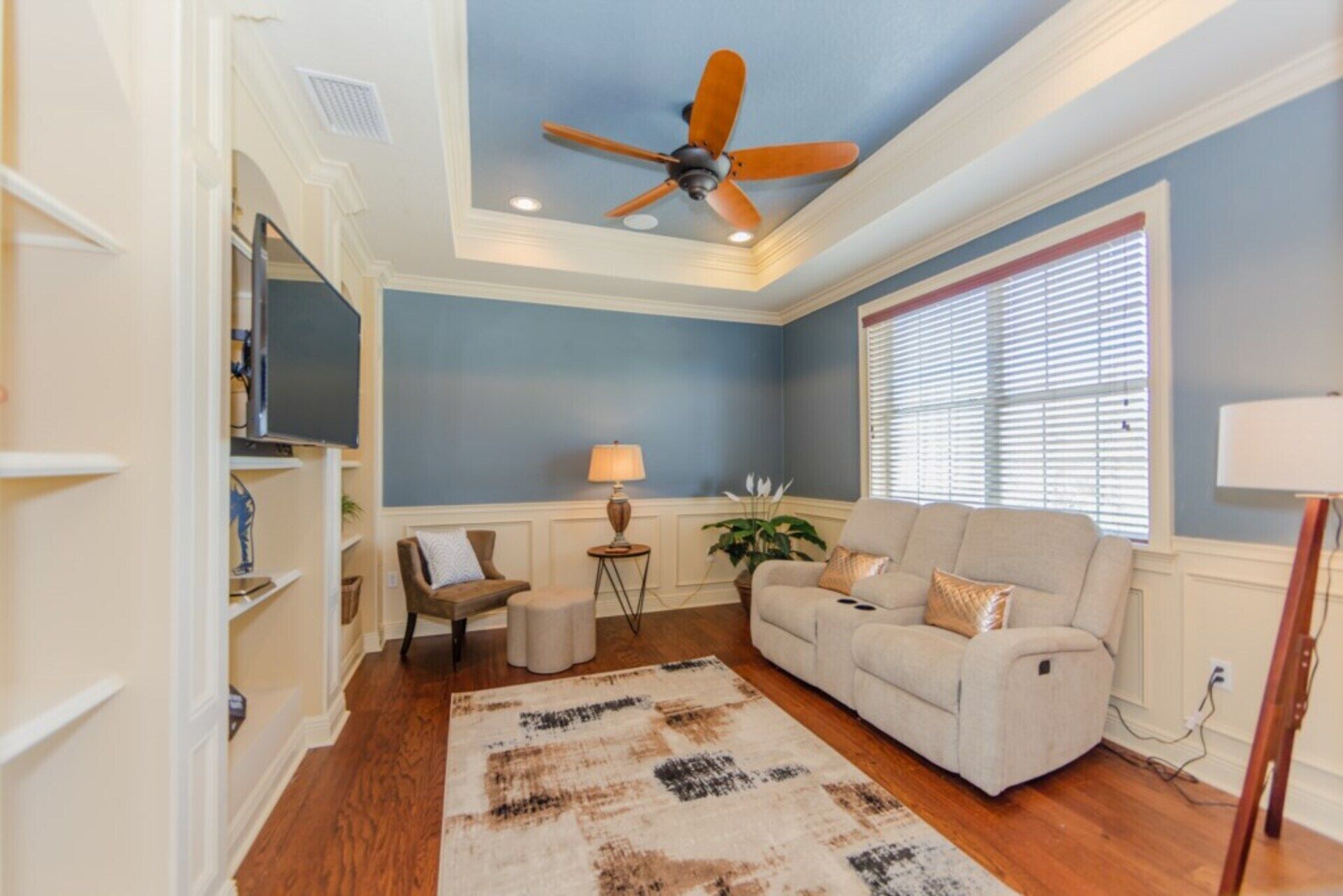 A living room with a ceiling fan, a sofa, a chair, a lamp, and a large window with blinds.