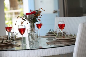 A dining table set with clear glasses, plates, and a centerpiece of red flowers and greenery. - Villa for Rent in Protaras 1051 (Paralimni)