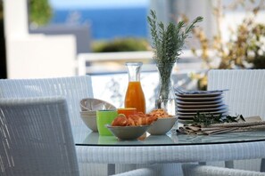 A table set with breakfast items, including croissants, a glass of orange juice, and a bottle of orange juice, with a view of the sea in the background. - Villa for Rent in Protaras 1051 (Paralimni)