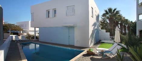 A modern white building with a swimming pool, a small garden, and a clear blue sky.