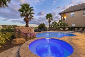 A swimming pool with a blue center, surrounded by lounge chairs and palm trees. - Rent a Luxury Villa on Reunion Resort, Minutes From Disney, Orlando Villa 3563 (Kissimmee)