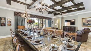 Une salle à manger spacieuse, avec une longue table dressée pour le repas, un lustre et une grande fenêtre agrémentée de rideaux.