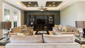 A modern living room with a large flat-screen TV, two sofas, a coffee table, and a ceiling fan.