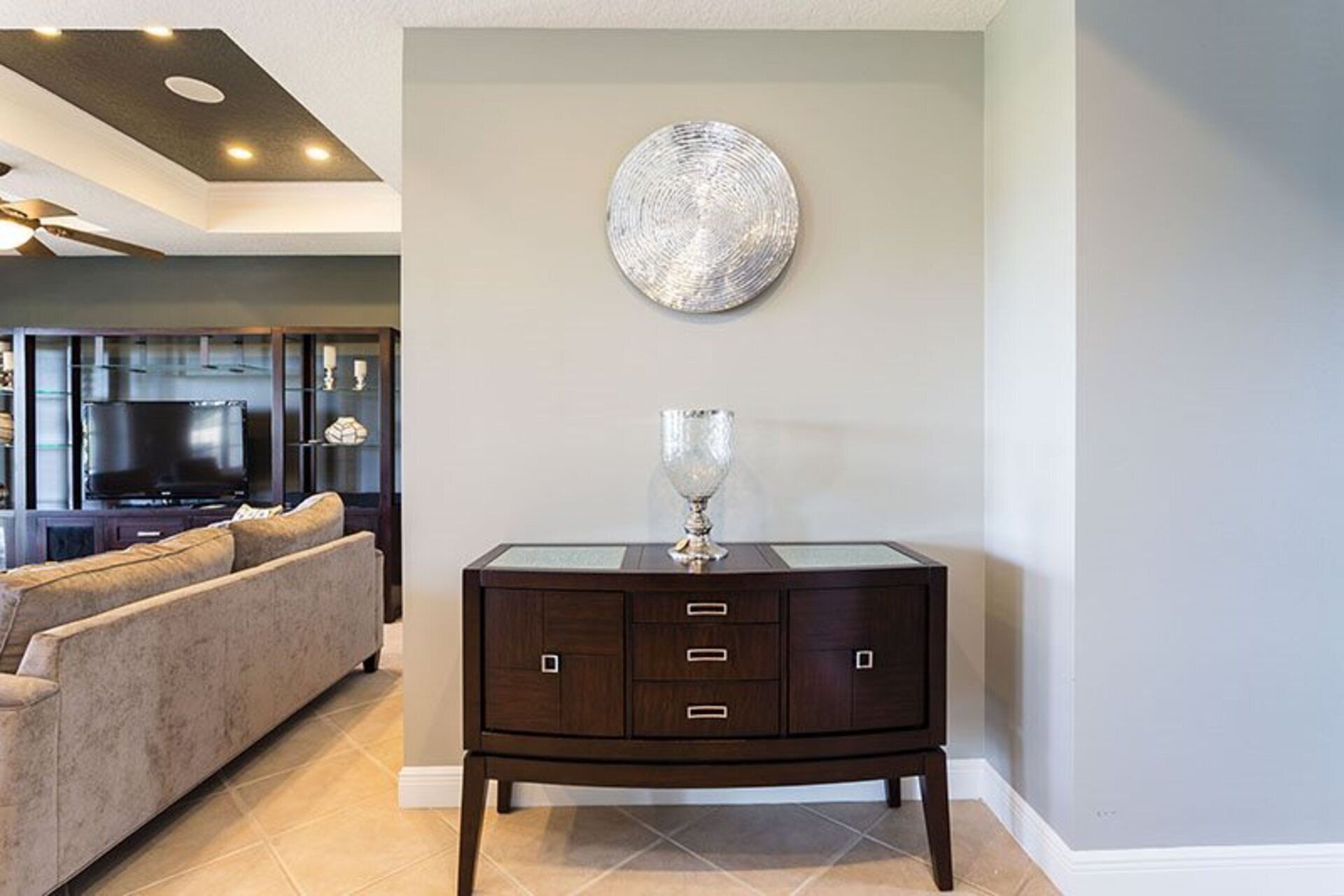 A modern living room with a dark wood cabinet, a glass-top coffee table, and a large abstract painting on the wall.