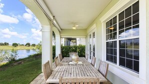 A covered patio with a wooden table and chairs, large windows, and a view of a lake.