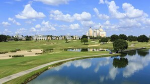 A golf course with a pond, a walking path, and a large hotel in the background.