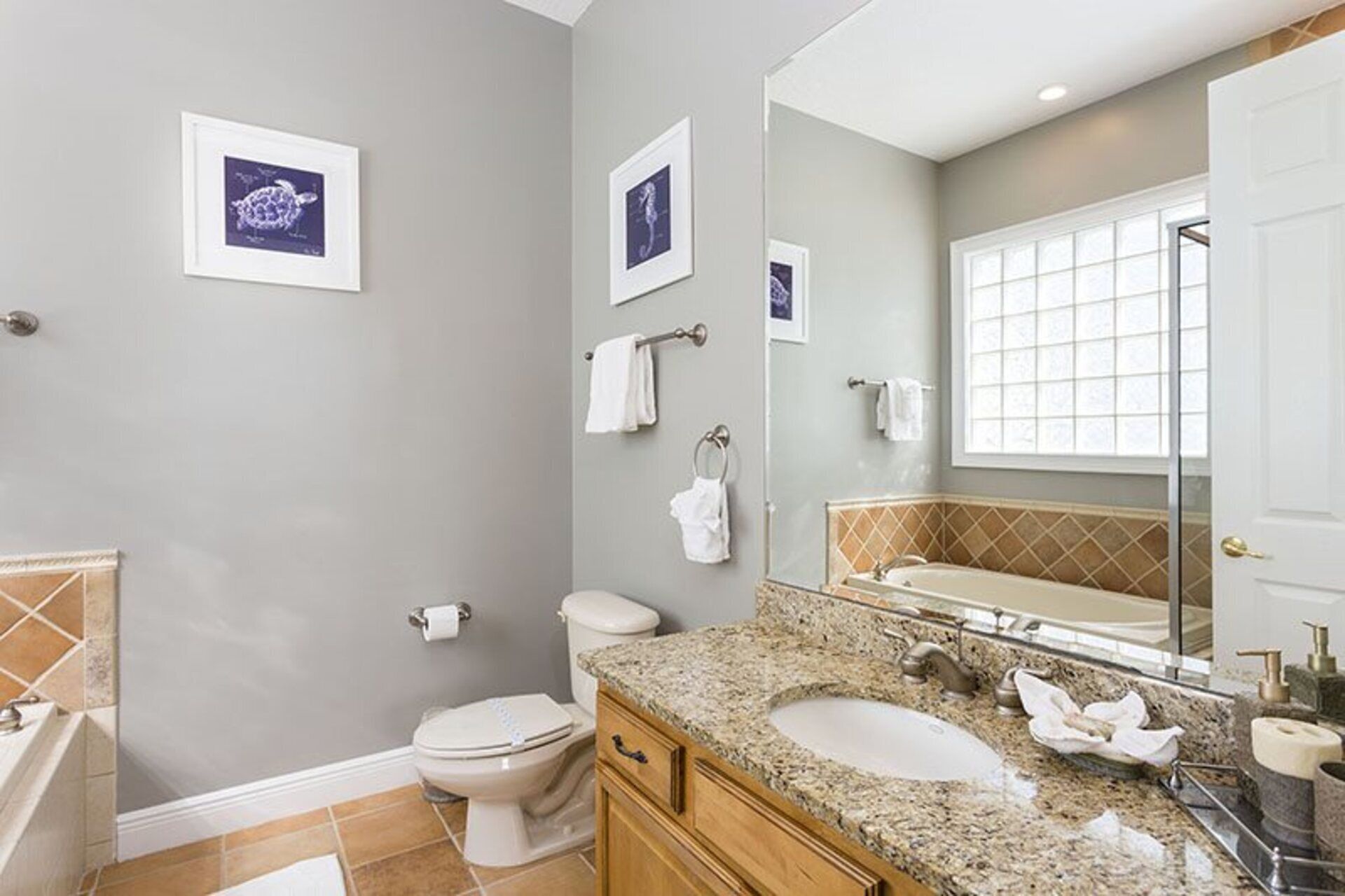 A bathroom with a toilet, sink, and mirror. There are towels hanging on the wall and a window with blinds.
