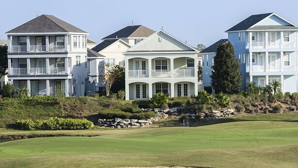 A row of beachfront houses with multiple stories, large windows, and balconies.