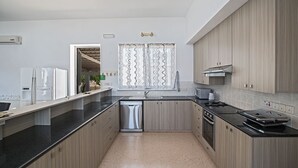 A modern kitchen with wooden cabinets, a black countertop, stainless steel appliances, and a window with a zigzag curtain.