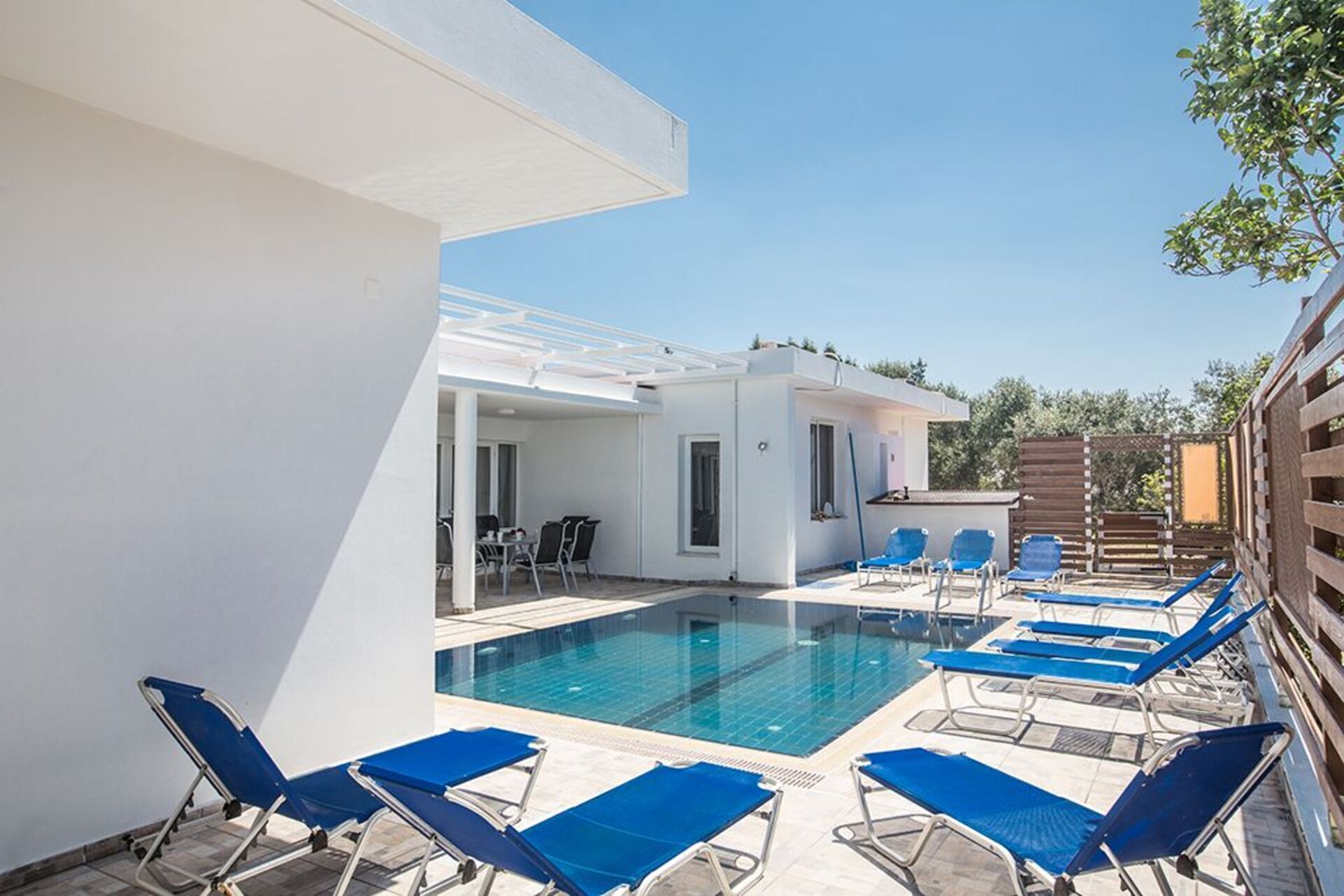 A pool area with blue lounge chairs and a small building with a patio.