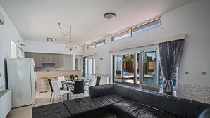 A modern living room with a black leather sofa, a dining area with a glass table, and a kitchen in the background.